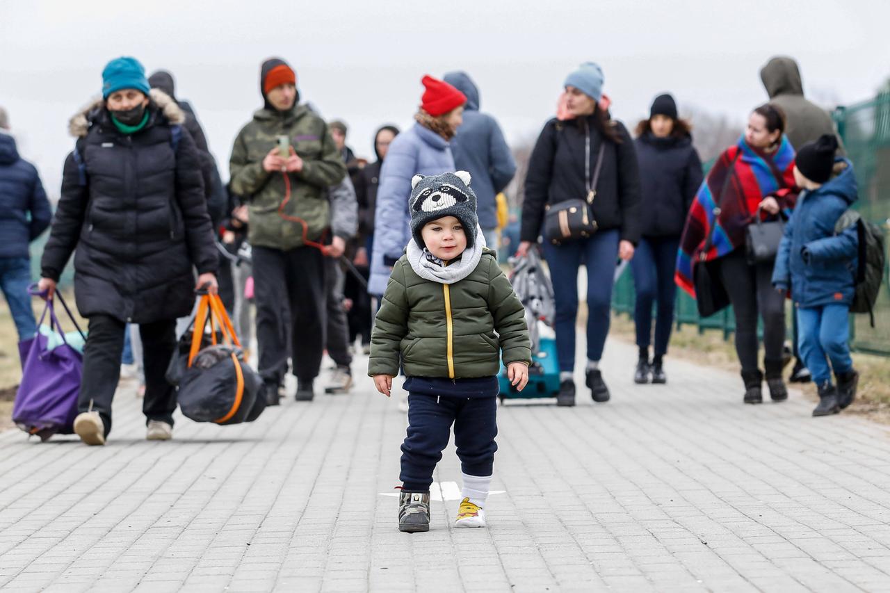 Familien mit Gepäck laufen auf einer Straße, im Vordergrund steht ein Kleinkind.