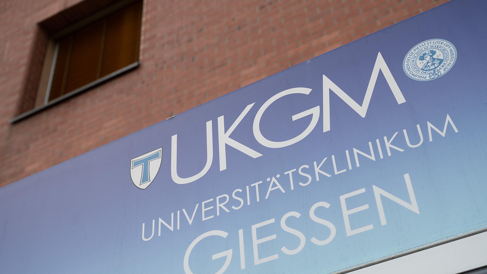 Der Schriftzug UKGM steht auf einem Schild, das an einer Ziegelsteinwand angebracht ist. Links und rechts neben dem UKGM stehen die Wappen der Justus-Liebig-Universität Gießen und der Philipps-Universität Marburg. Darunter steht Universitätsklinikum Gießen. Der Schriftzug UKGM steht auf einem Schild, das an einer Ziegelsteinwand angebracht ist. Links und rechts neben dem UKGM stehen die Wappen der Justus-Liebig-Universität Gießen und der Philipps-Universität Marburg. Darunter steht Universitätsklinikum Gießen.