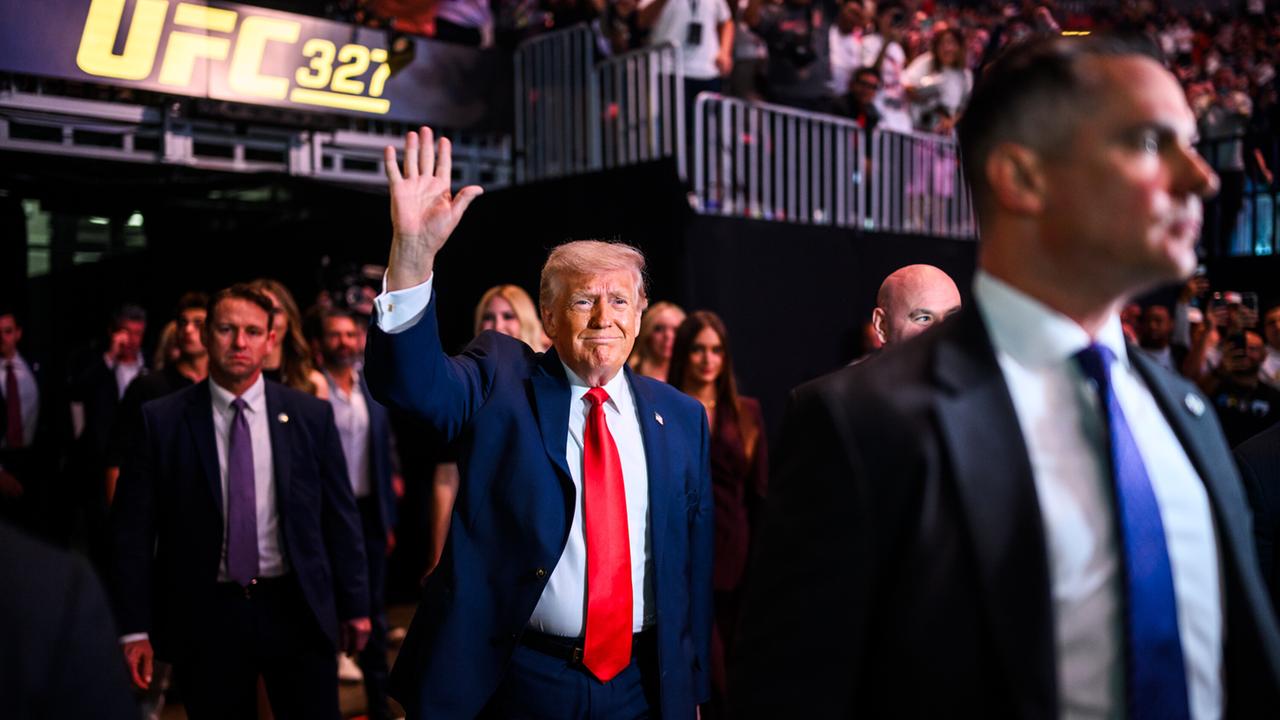 US-Präsident Donald Trump zieht ins Kaseya Center in Miami, Florida zu einem Kampfsportevent der UFC an der Seite von UFC-Chef Dana White ein. Trump trägt einen roten Schlips und einen blauen Anzug und winkt. 11. April 2026