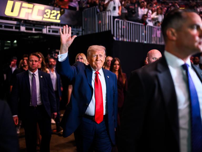 US-Präsident Donald Trump zieht ins Kaseya Center in Miami, Florida zu einem Kampfsportevent der UFC an der Seite von UFC-Chef Dana White ein. Trump trägt einen roten Schlips und einen blauen Anzug und winkt. 11. April 2026 US-Präsident Donald Trump zieht ins Kaseya Center in Miami, Florida zu einem Kampfsportevent der UFC an der Seite von UFC-Chef Dana White ein. Trump trägt einen roten Schlips und einen blauen Anzug und winkt. 11. April 2026