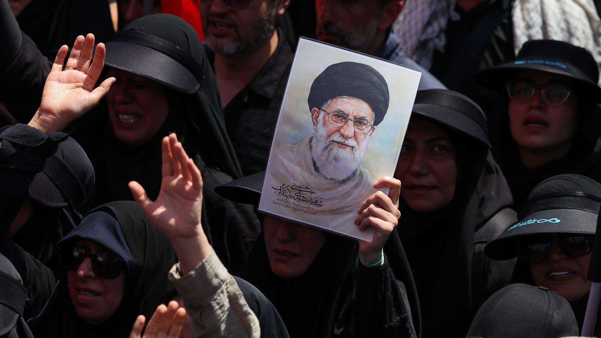 Dunkel gekleidete Menschen bei einem Trauerzug für den getöteten Obersten Führer des Iran, Ajatollah Ali Chamenei. Eine der Person hält ein Bild Chemeneis. Dunkel gekleidete Menschen bei einem Trauerzug für den getöteten Obersten Führer des Iran, Ajatollah Ali Chamenei. Eine der Person hält ein Bild Chemeneis.