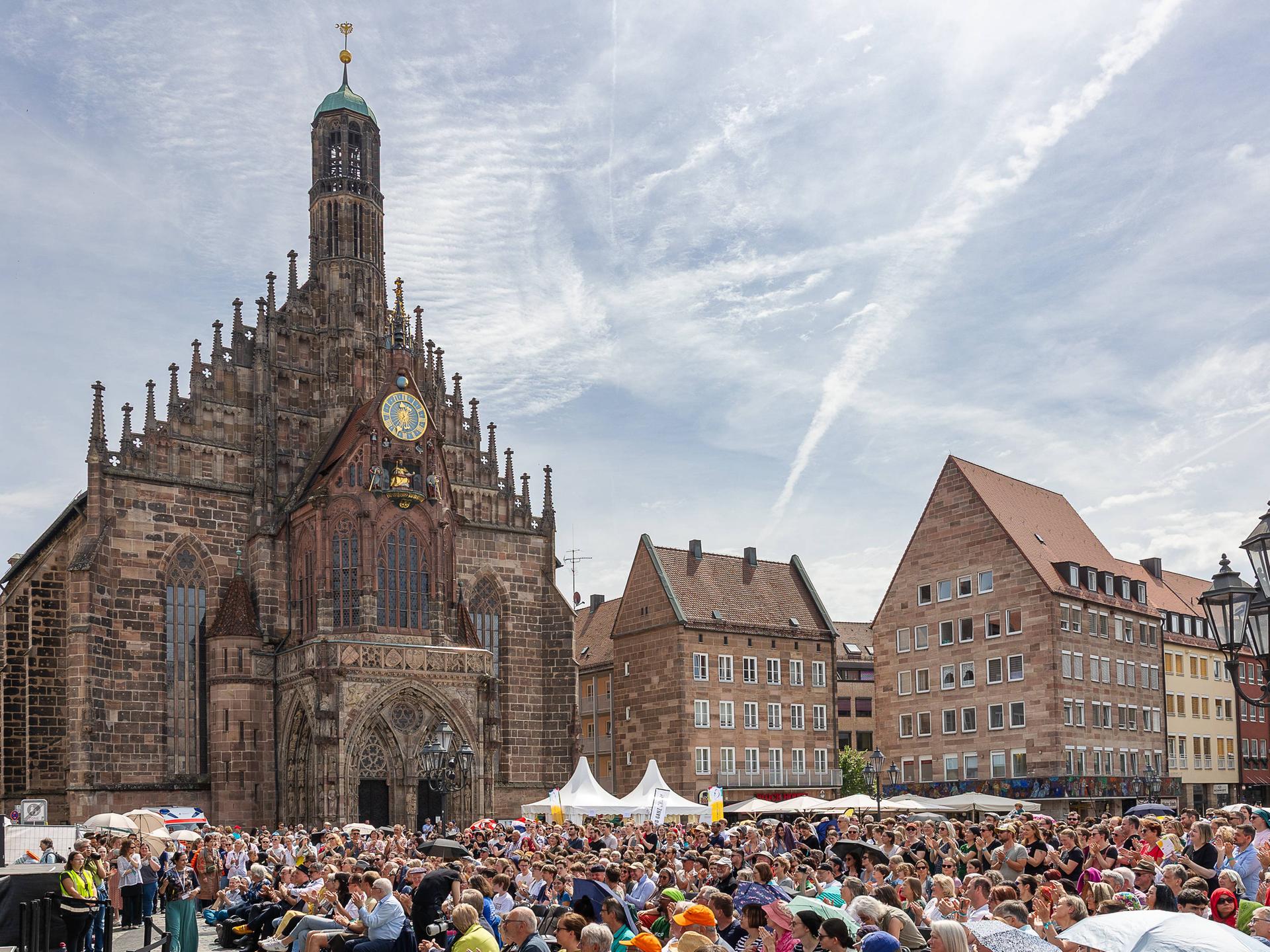 Blick auf einen sommerlichen, dicht besetzten Platz in der Altstadt von Nürnberg mit seinen markanten historischen Gebäuden. 