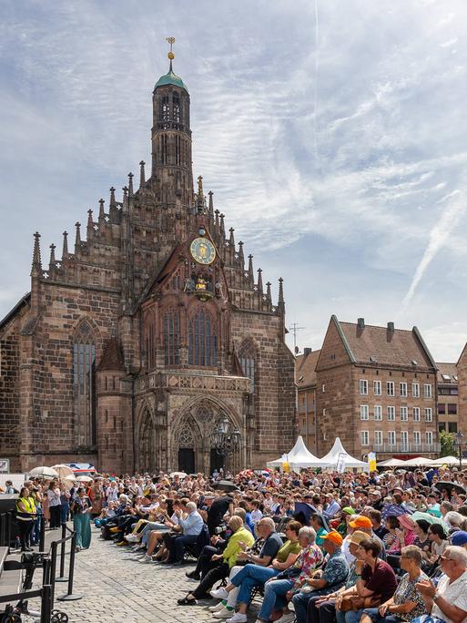 Blick auf einen sommerlichen, dicht besetzten Platz in der Altstadt von Nürnberg mit seinen markanten historischen Gebäuden. 