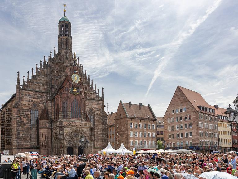 Blick auf einen sommerlichen, dicht besetzten Platz in der Altstadt von Nürnberg mit seinen markanten historischen Gebäuden. 