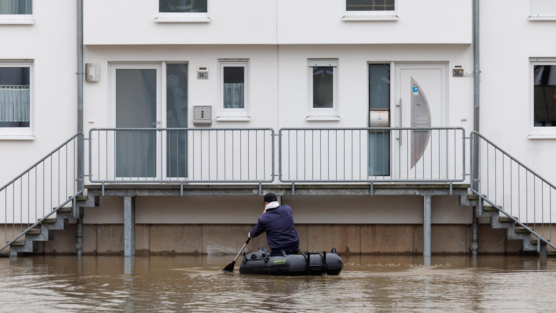 Ein Mann sitzt in einem Schlauchboot und paddelt zu einem Haus, das im Wasser steht.