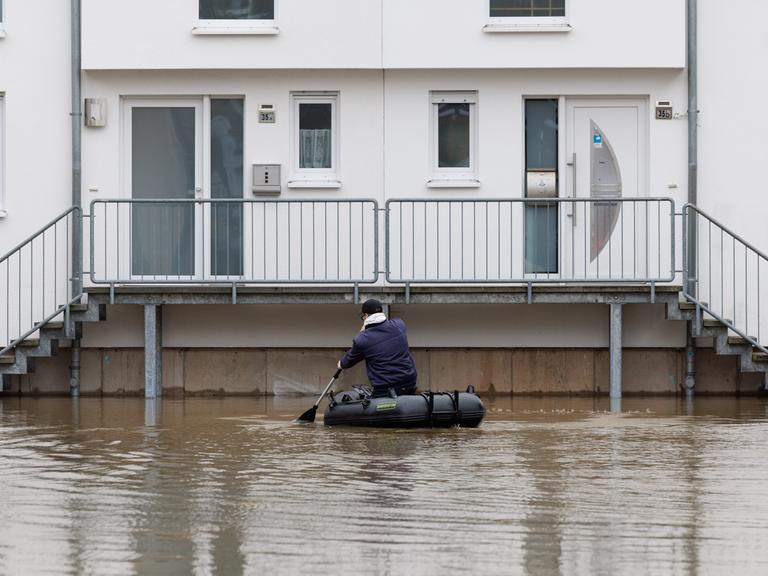 Ein Mann sitzt in einem Schlauchboot und paddelt zu einem Haus, das im Wasser steht.