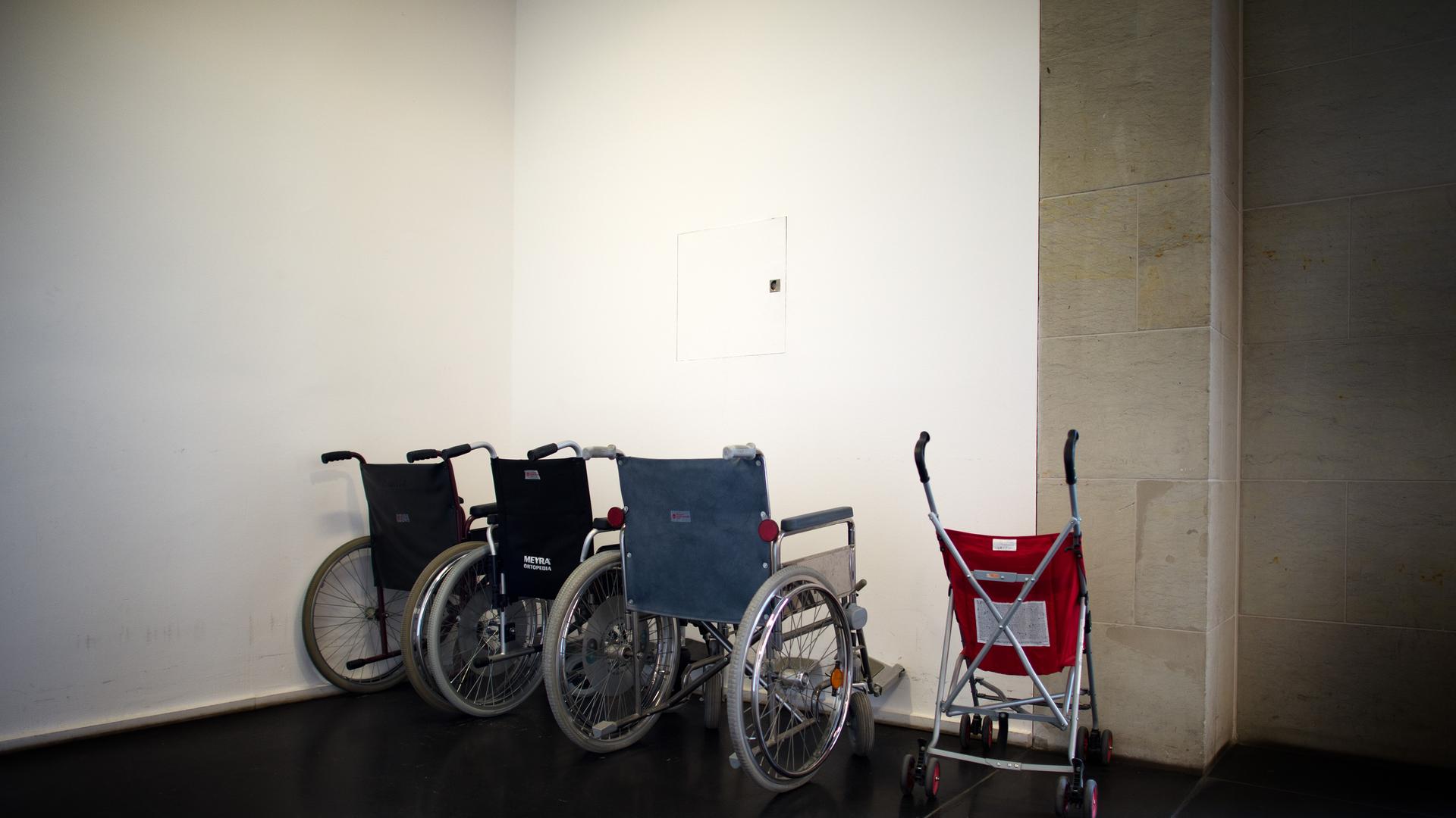 Ein Kinder-Buggy steht neben mehreren Rollstühlen in einem Treppenhaus.