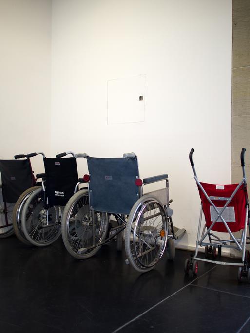 Ein Kinder-Buggy steht neben mehreren Rollstühlen in einem Treppenhaus.