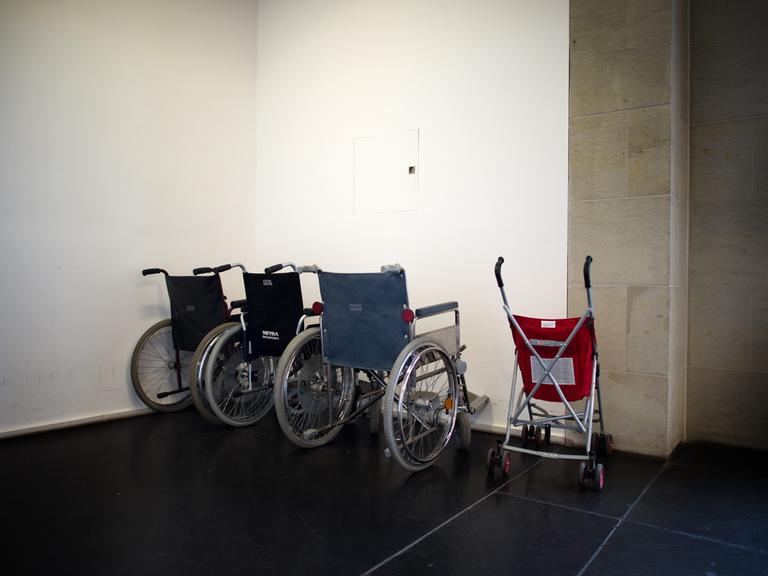 Ein Kinder-Buggy steht neben mehreren Rollstühlen in einem Treppenhaus.