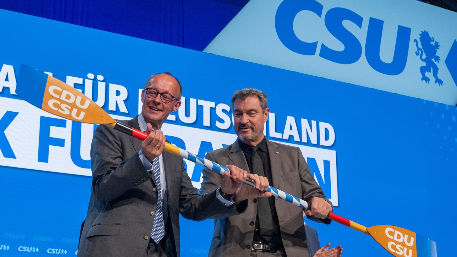 Friedrich Merz (l), CDU-Bundesvorsitzender und Unionsfraktionsvorsitzender, bekommt auf dem CSU-Parteitag von Markus Söder (r), Vorsitzender der CSU, auf der Bühne ein Paddel mit dem Logo der beiden Parteien überreicht.