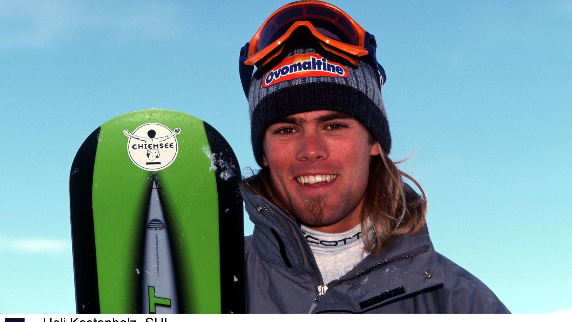 Ueli Kestenholz hält ein Snowboard und lächelt in die Kamera.