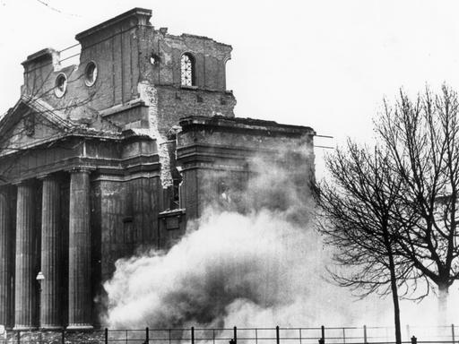 Historisches Schwarzweißfoto einer ruinösen Synagoge, die gesprengt wird.