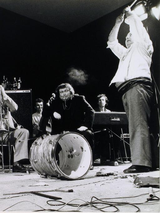 Eine Gruppe von Musikern an ihren Instrumenten, während einer von ihnen auf eine am Boden liegende Trommel einschlägt