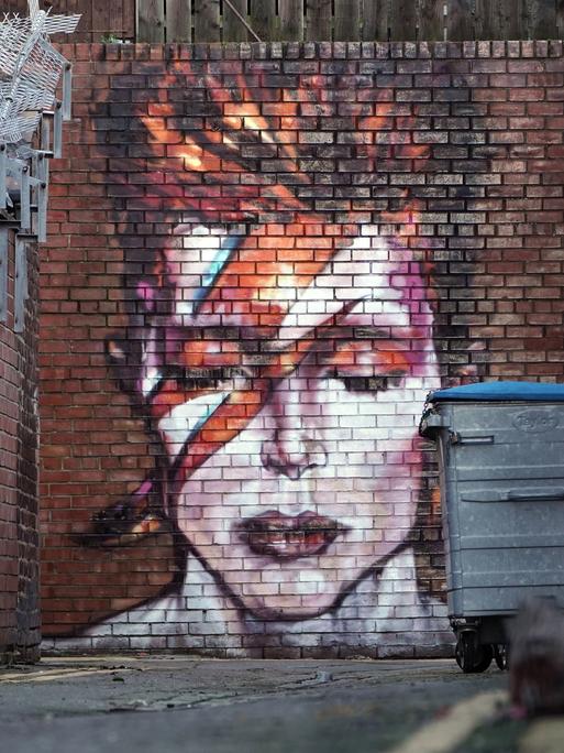 Ein Graffito in einem Hinterhof zeigt David Bowie mit geschlossenen Augen und den für ihn typischen Blitz im Gesicht.