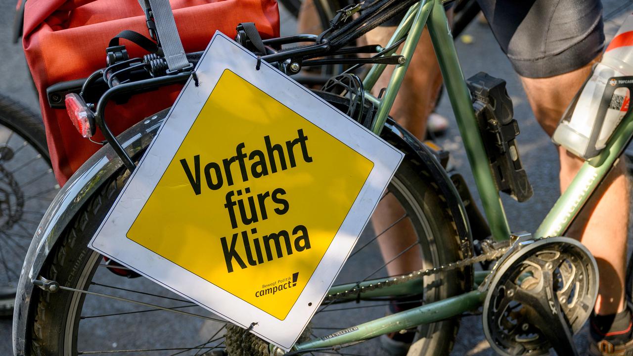 Hauptstraßeschild mit Aufschrift "Vorfahrt fürs Klima" ist vor dem Hinterrad eines Fahrrads befestigt.
