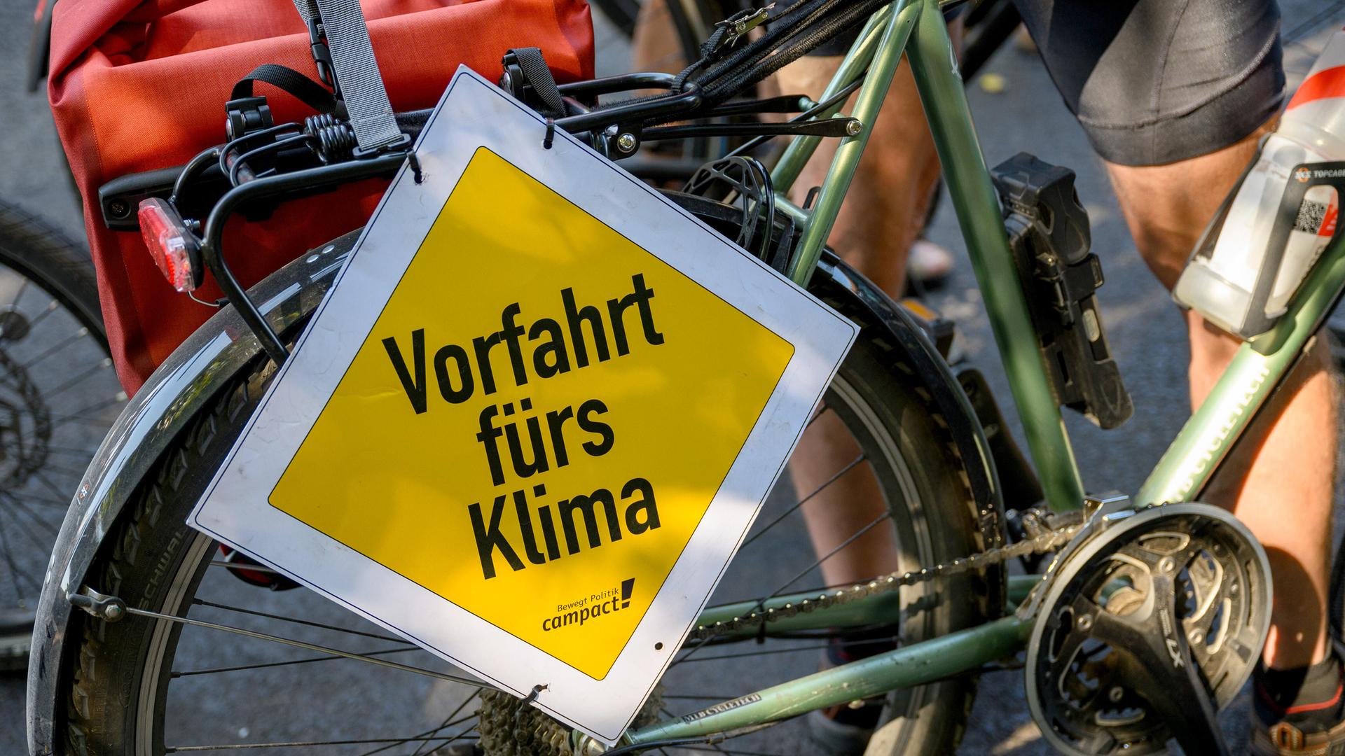 Hauptstraßeschild mit Aufschrift "Vorfahrt fürs Klima" ist vor dem Hinterrad eines Fahrrads befestigt.