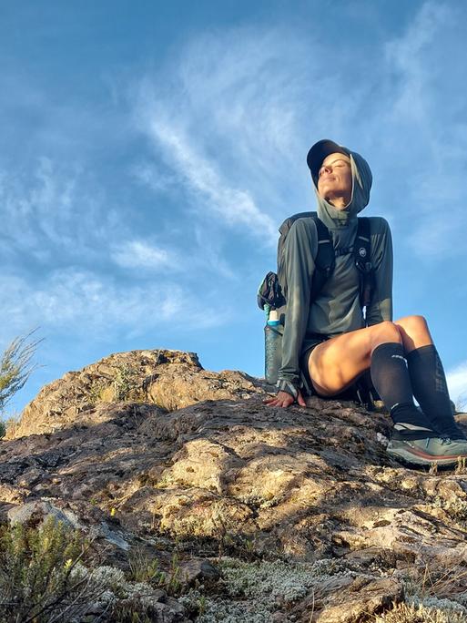 Eine Frau in Wanderkleidung sitzt auf einem Felsen und blickt in die Sonne. Eine Frau in Wanderkleidung sitzt auf einem Felsen und blickt in die Sonne.