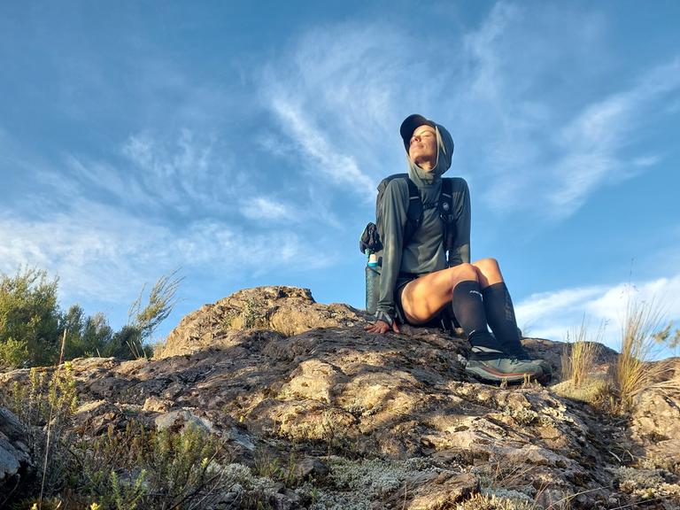 Eine Frau in Wanderkleidung sitzt auf einem Felsen und blickt in die Sonne. Eine Frau in Wanderkleidung sitzt auf einem Felsen und blickt in die Sonne.