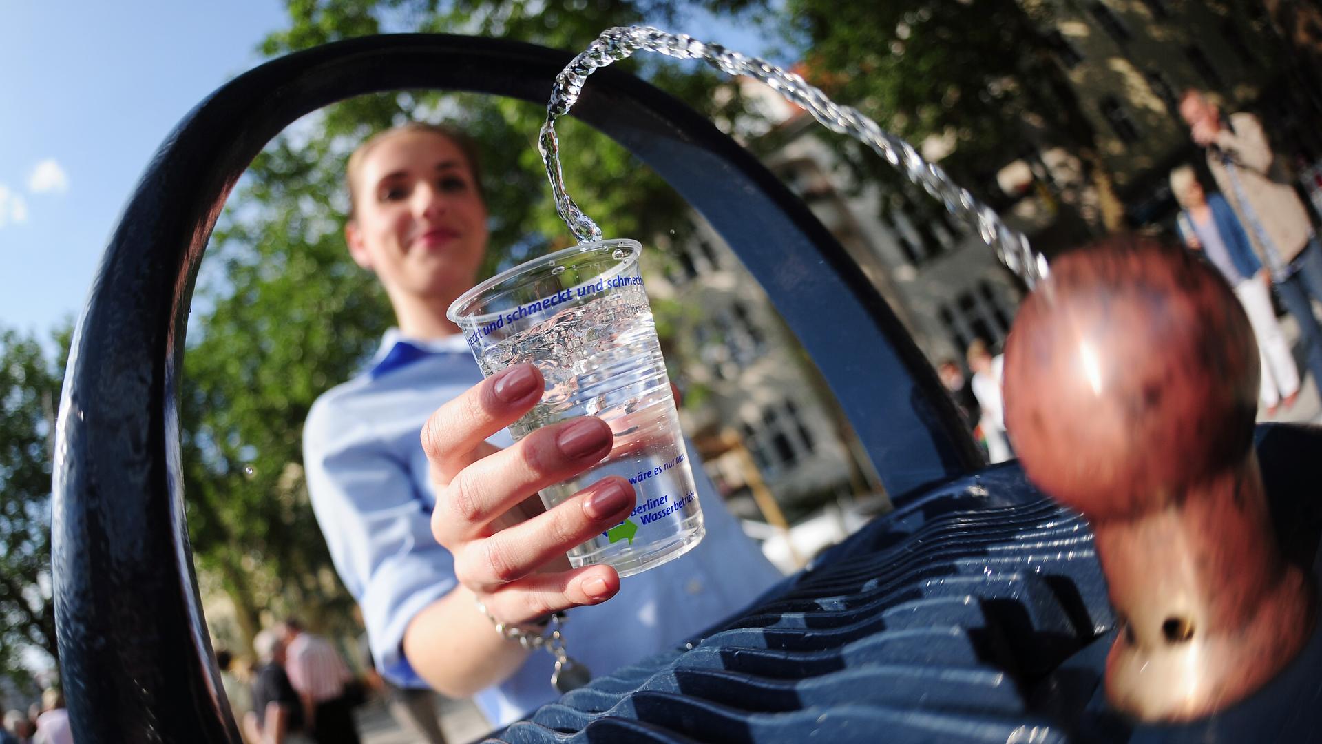 Eine junge Frau schöpft Wasser aus einem Trinkbrunnen. 