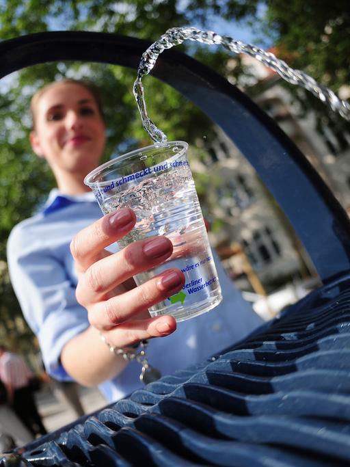 Eine junge Frau schöpft Wasser aus einem Trinkbrunnen. 