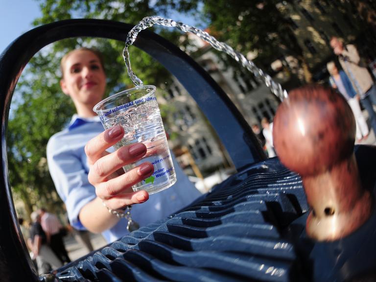 Eine junge Frau schöpft Wasser aus einem Trinkbrunnen. 