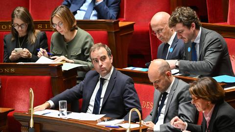 Lecornu im schwarzen Jackett sitzt auf einer der roten Regierungsbänke. Neben und hinter ihm weitere Politiker. 