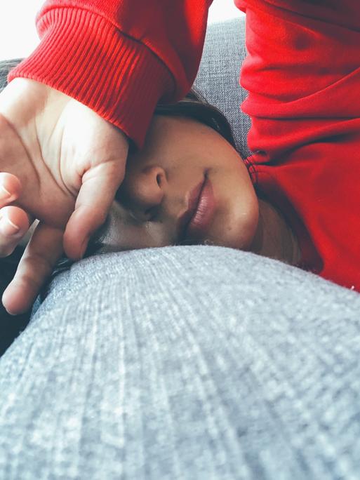 Eine Frau mit rotem Sweater liegt auf dem Sofa und hält sich die Hand vor die Augen.