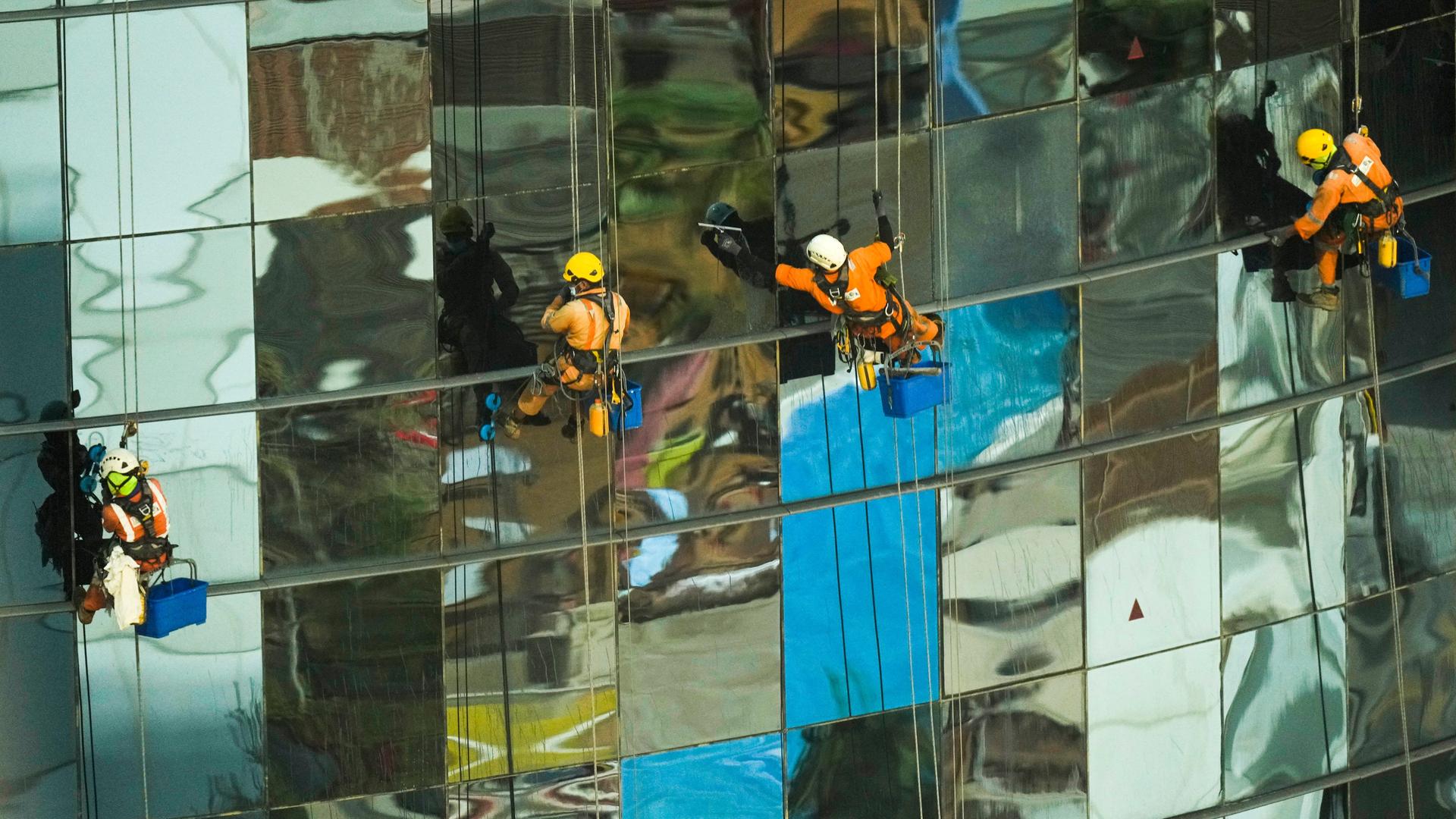 Gastarbeiter hängen an Sicherungen an der Außenfassade eines Gebäudes im West Bay-Viertel in Doha und putzen die Fensterscheiben.