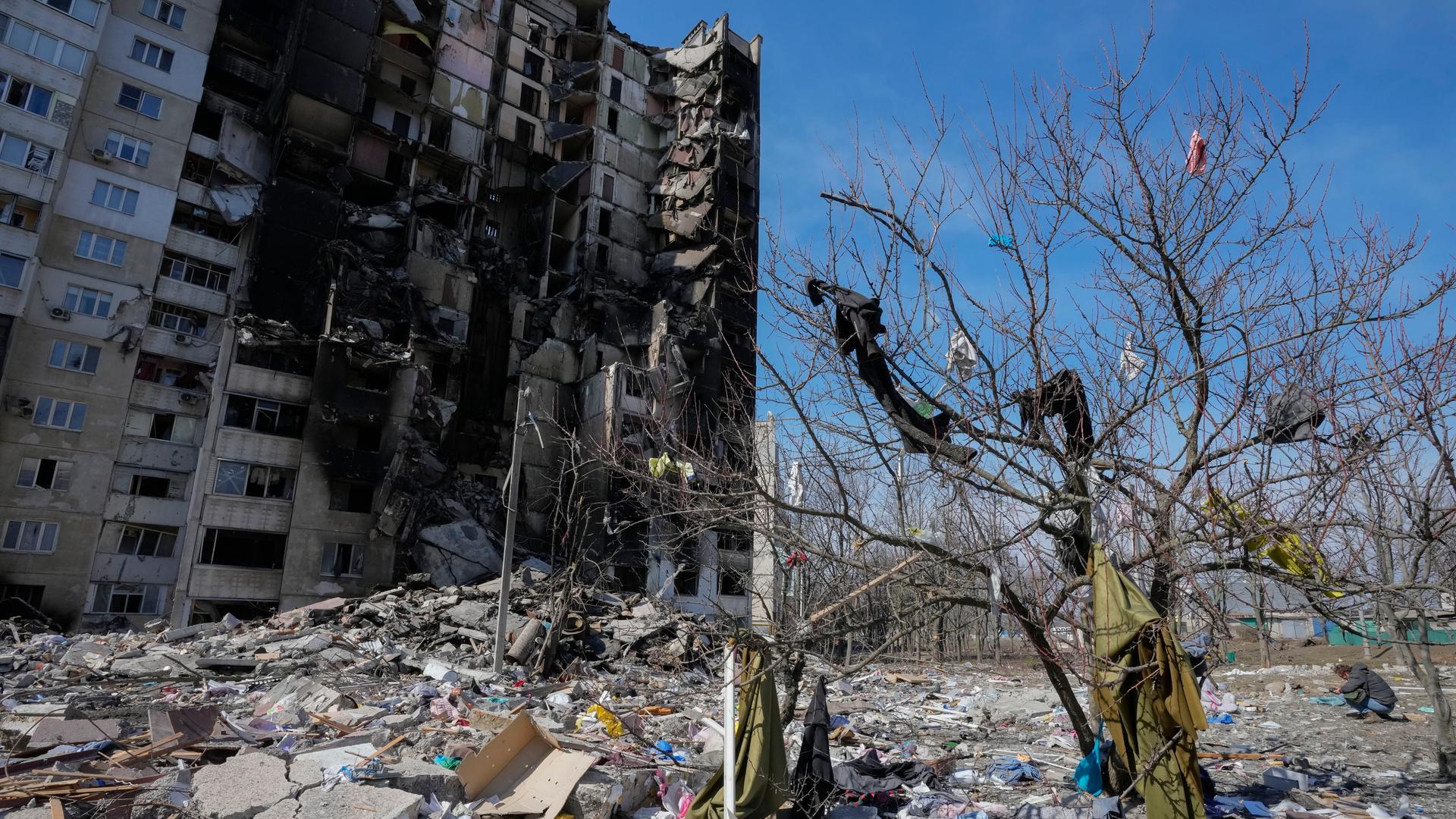 Kleidung, die durch russischen Beschuss aus einem ausgebrannten Haus in Charkiw in der Ostukraine auf einen Baum geschleudert wurde, und dahinter das bombardierte Haus am 26. März 2022.