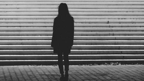 Eine Frau steht vor einer Treppe. Es ist nur ihre Silhouette zu erkennen.