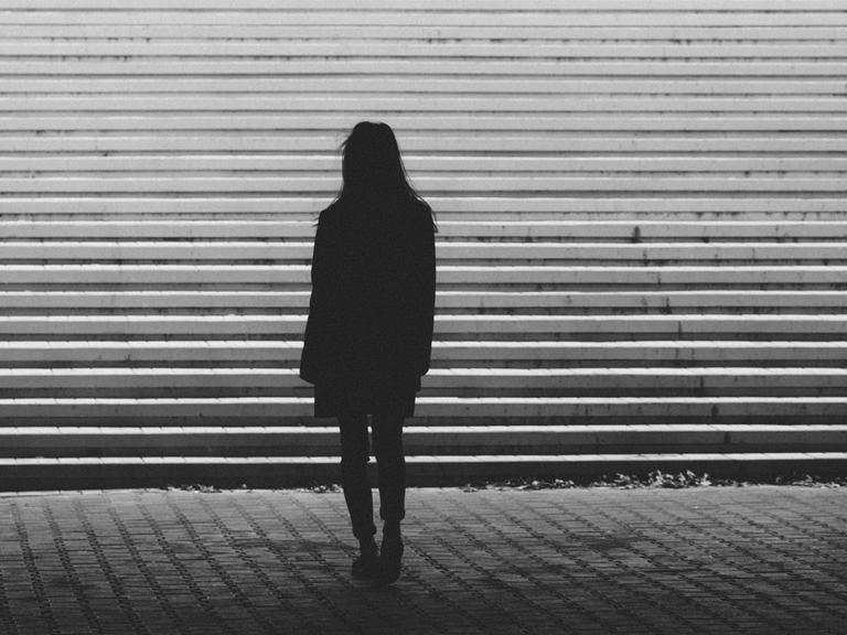 Eine Frau steht vor einer Treppe. Es ist nur ihre Silhouette zu erkennen.