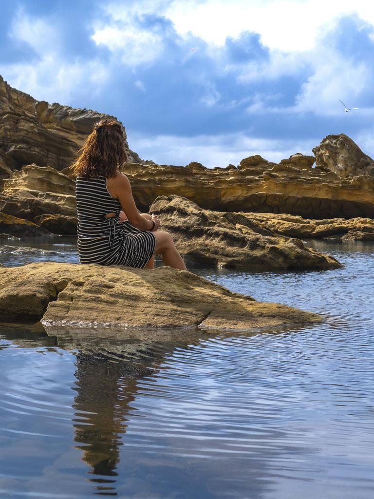 Frau sitzt auf alten Felsen an einem ruhigen Flutbecken, beobachtet das ruhige Meer und die zerklüftete Küste des Mount Jaizkibel im Baskenland und findet Einsamkeit in der Natur. 