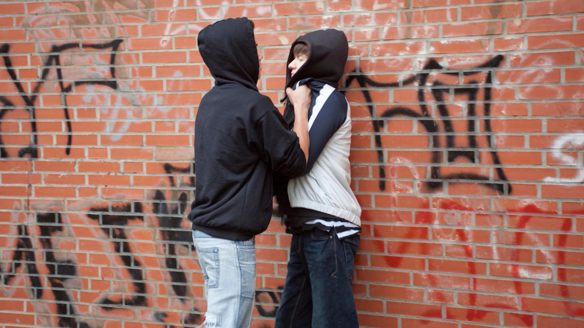 Ein Teenager drückt einen kleineren gewaltsam gegen eine Wand (gestellte Szene).