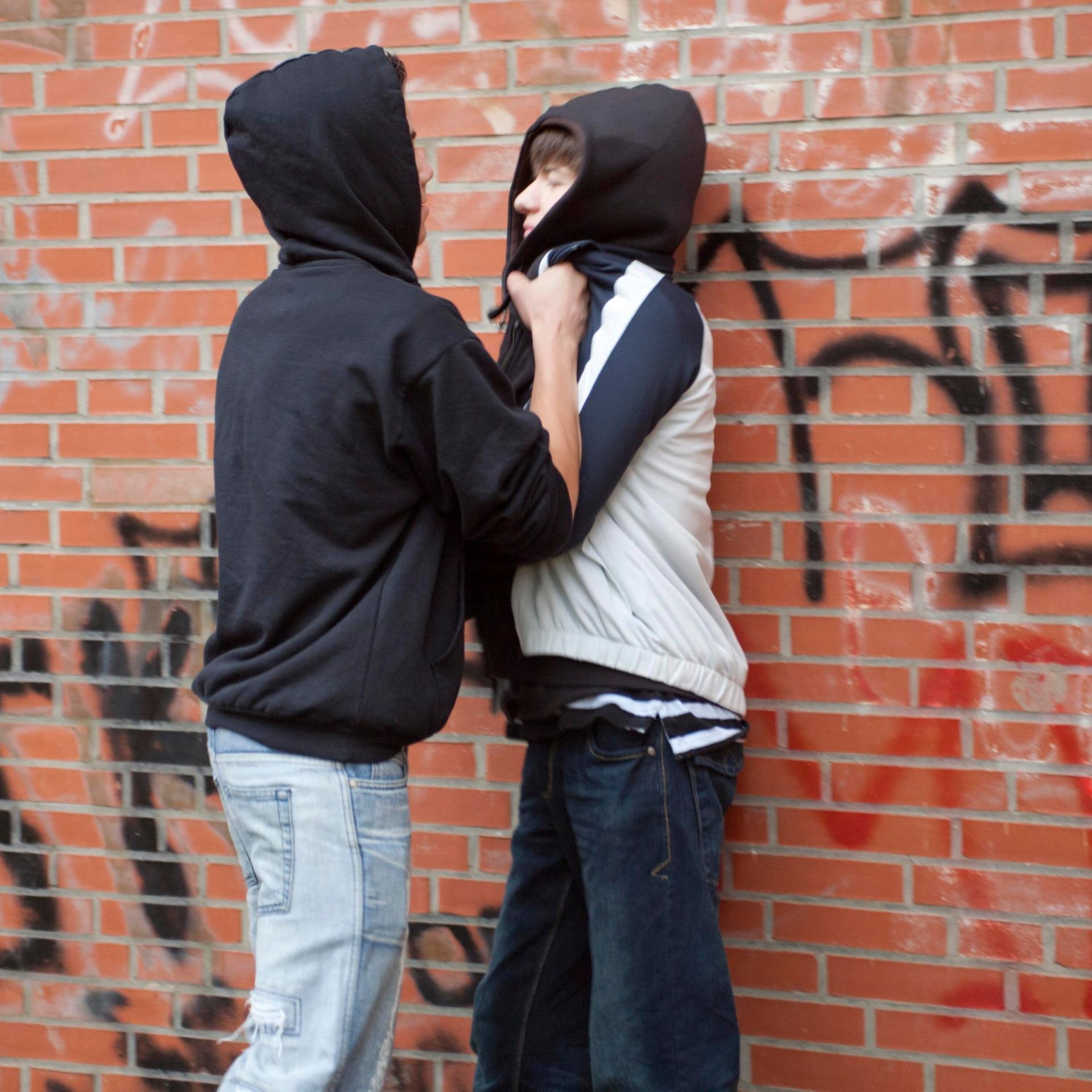 Ein Teenager drückt einen kleineren gewaltsam gegen eine Wand (gestellte Szene)