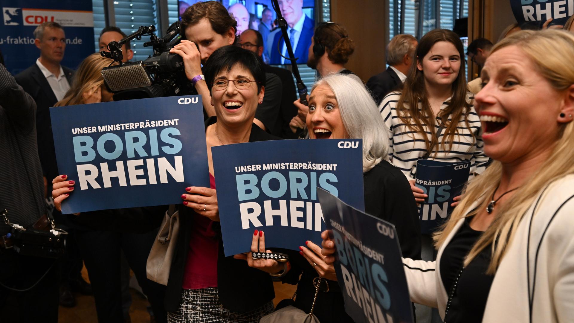 Anhänger des hessischen Ministerpräsidentens Rhein halten auf der CDU-Wahlparty nach der Veröffentlichung der ersten Prognose zur Landtagswahl in Hessen Schilder mit seinem Namen. Anhänger des hessischen Ministerpräsidentens Rhein halten auf der CDU-Wahlparty nach der Veröffentlichung der ersten Prognose zur Landtagswahl in Hessen Schilder mit seinem Namen.
