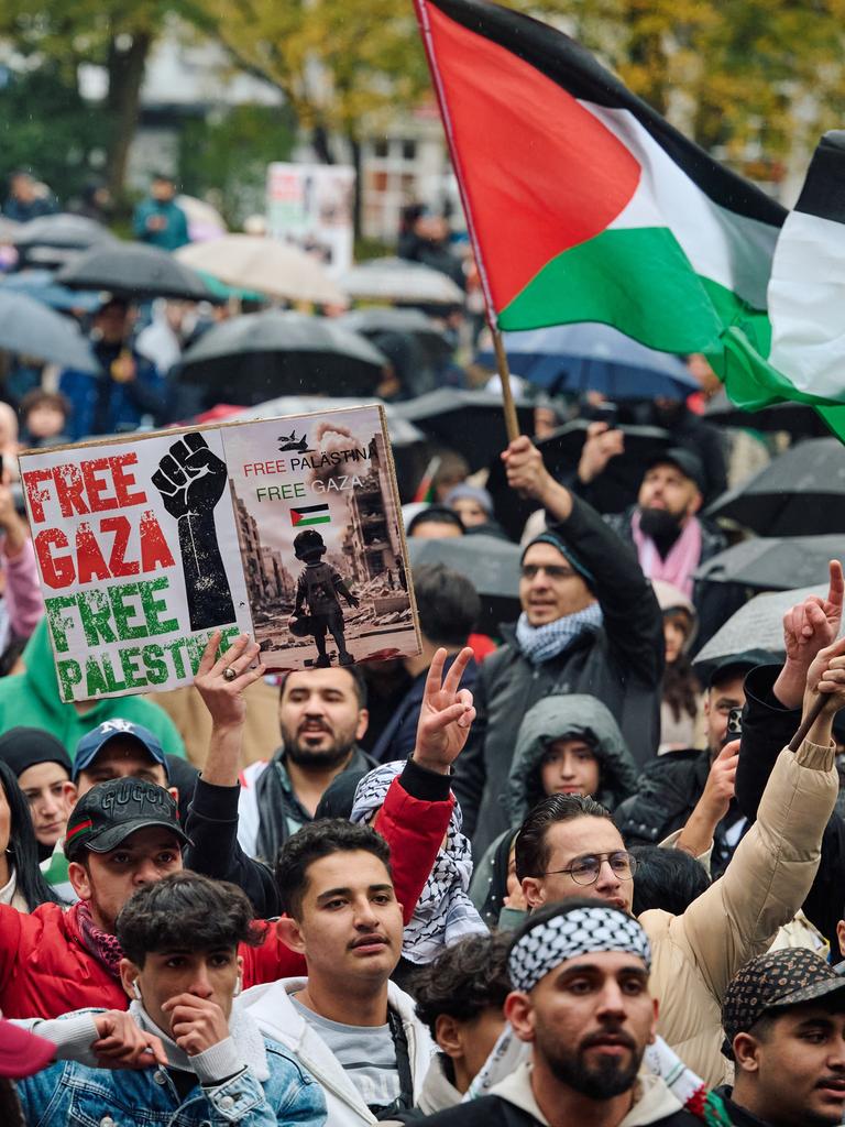 Teilnehmer einer propalästinensischen Demo schwenken Fahnen und halten Schilder hoch.