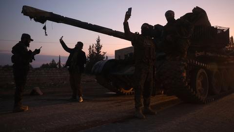 Im Abendrot stehen mehrere Männner vor einem Panzer und machen Selfies mit Mobiltelefonen. Sie sind als Silhouetten zu sehen. 
