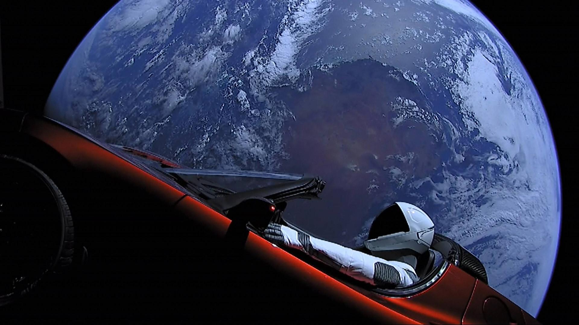 Roter Tesla Roadster im Weltraum mit der Erde im Hintergrund und einem Raumfahrer auf dem Fahrersitz