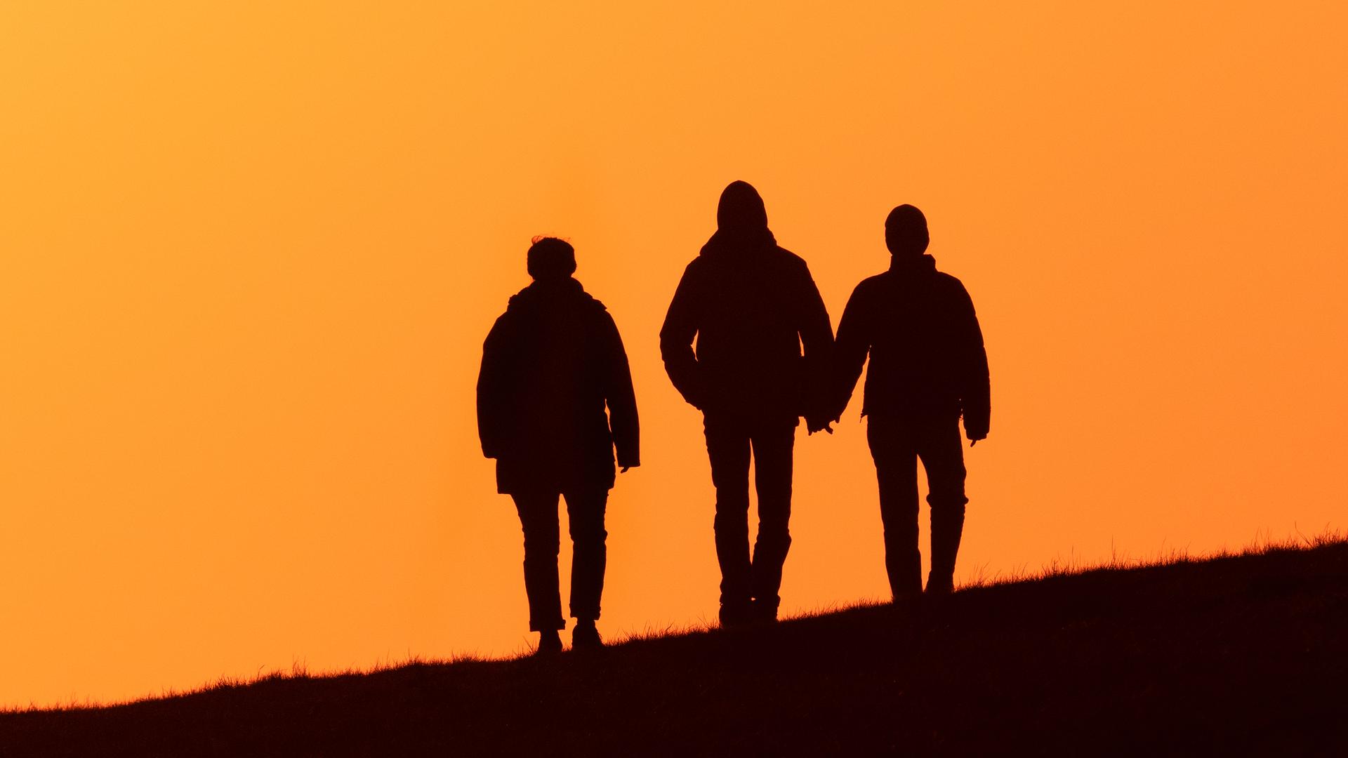 Drei Menschen spazieren abends im Gegenlicht der Abendsonne auf dem Deich Drei Menschen spazieren abends im Gegenlicht der Abendsonne auf dem Deich