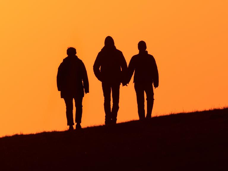 April 2023 auf Wangerooge: ältere Frau und ein junges Paar spazieren abends im Gegenlicht der Abendsonne auf dem Deich 