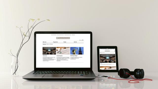 Auf einem Schreibtisch liegen ein Laptop, ein Tablet, sowie ein Smartphone mit Kopfhörern.