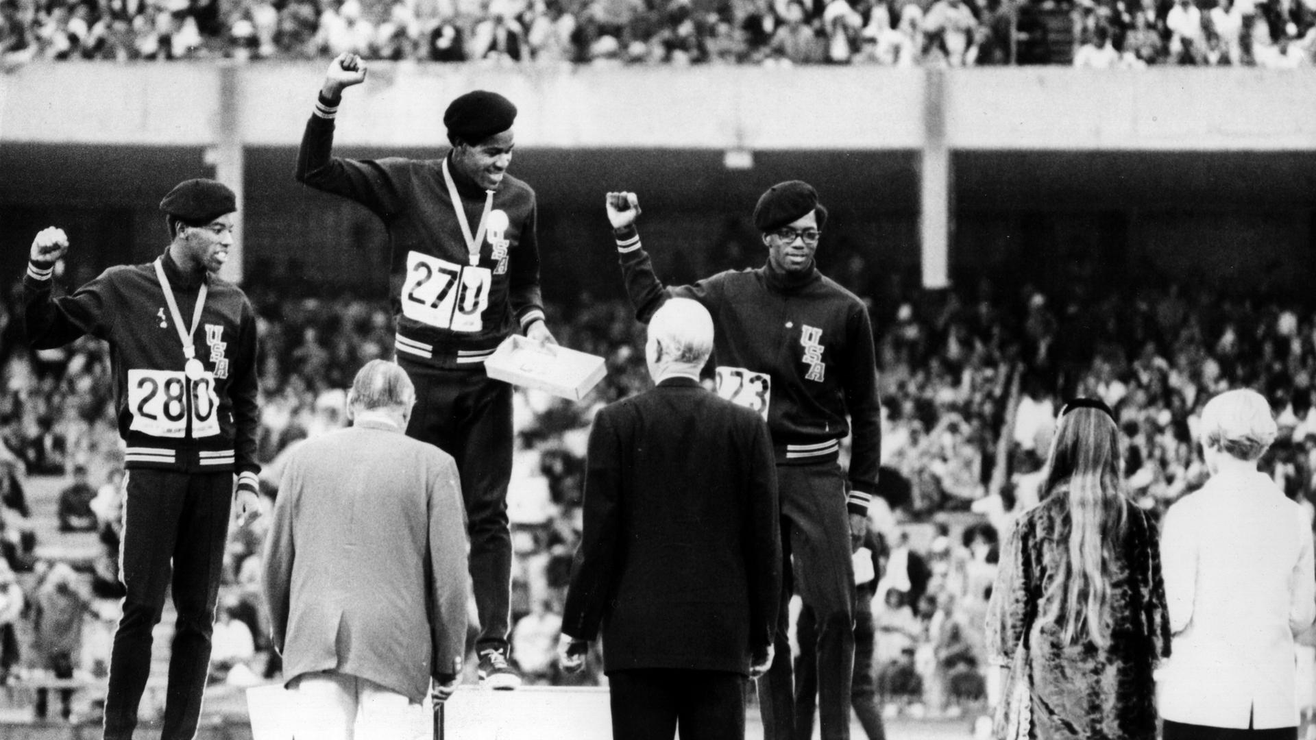 Die farbigen US-amerikanischen Sportler Larrie James (Silber), Lee Evans (Gold) und Ron Freeman (Bronze) strecken während der Siegerehrung über 400 Meter die geballte rechte Faust, das Zeichen der "Black Power" Bewegung, in die Höhe. 