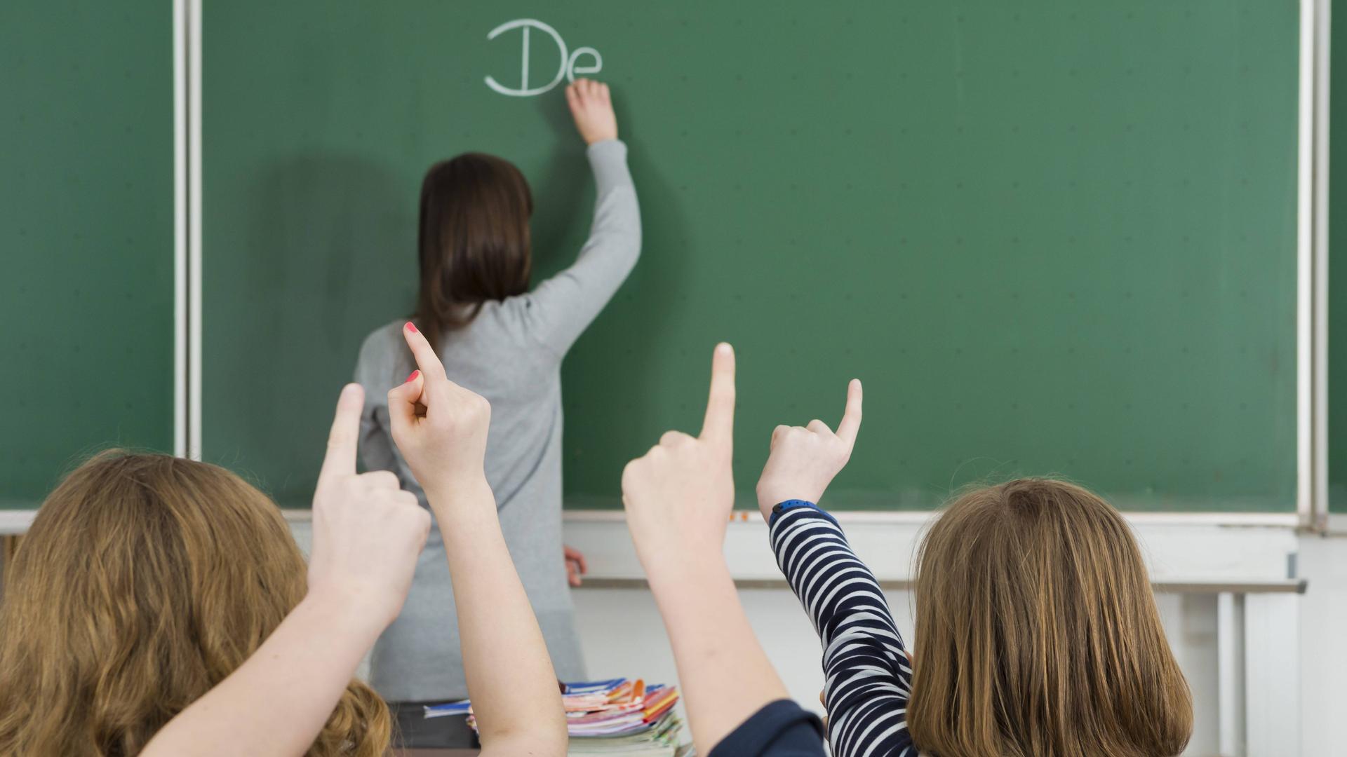 Klassenzimmer mit Tafel, Schüler melden sich.