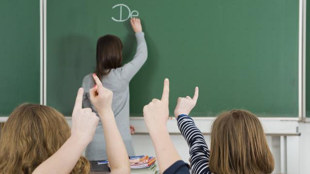 Klassenzimmer mit Tafel, Schüler melden sich.