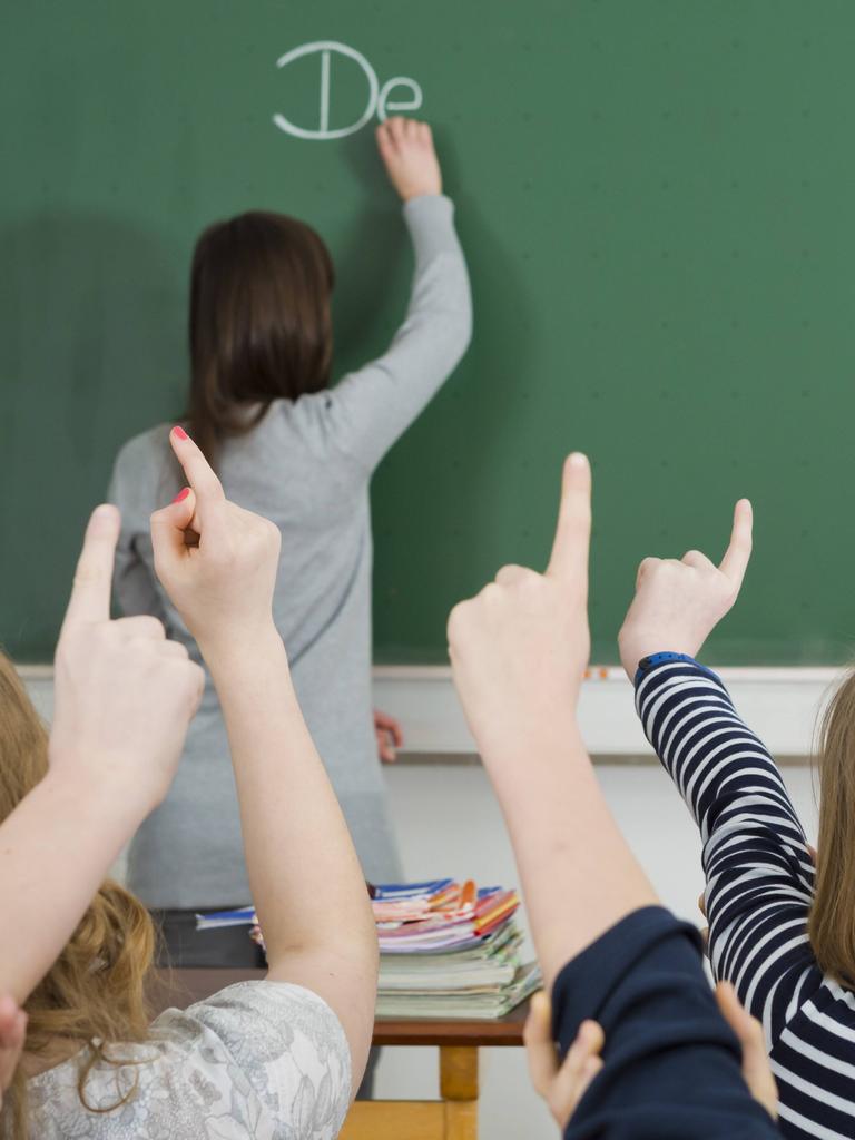 Klassenzimmer mit Tafel, Schüler melden sich.