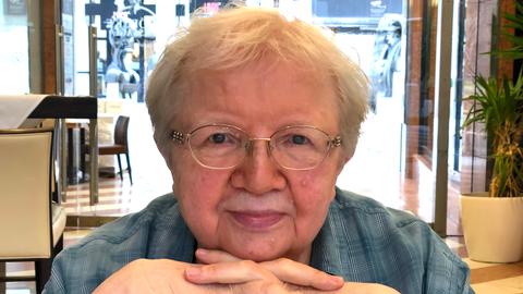 Luise F. Pusch. Eine ältere Frau mit Brille und kurzen Haaren sitzt an einem Tisch. 