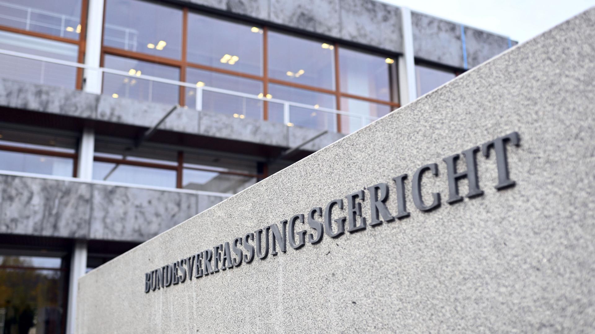 Aussenaufnahme des Bundesverfassungsgerichts in Karlsruhe. Ein grauer Betonbau, im Vordergrund ist eine Mauer auf der "Bundesverfassungsgericht" steht.