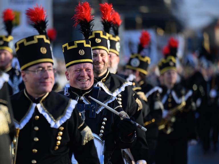 Teilnehmer der Bergparade gehen nebeneinander. Sie sind in traditioneller Bergmanns-Uniform gekleidet.