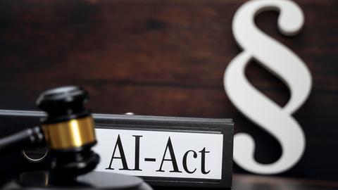 Ein Richterhammer, Paragraphen-Symbol und ein Ordner mit der Aufschrift AI-Act sind in einer Fotomontage zusammengesetzt.