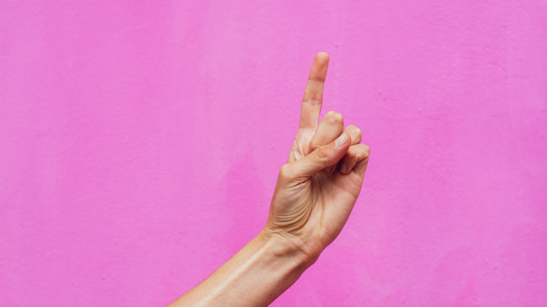 Ein erhobener Zeigefinger vor pinkem Hintergrund.